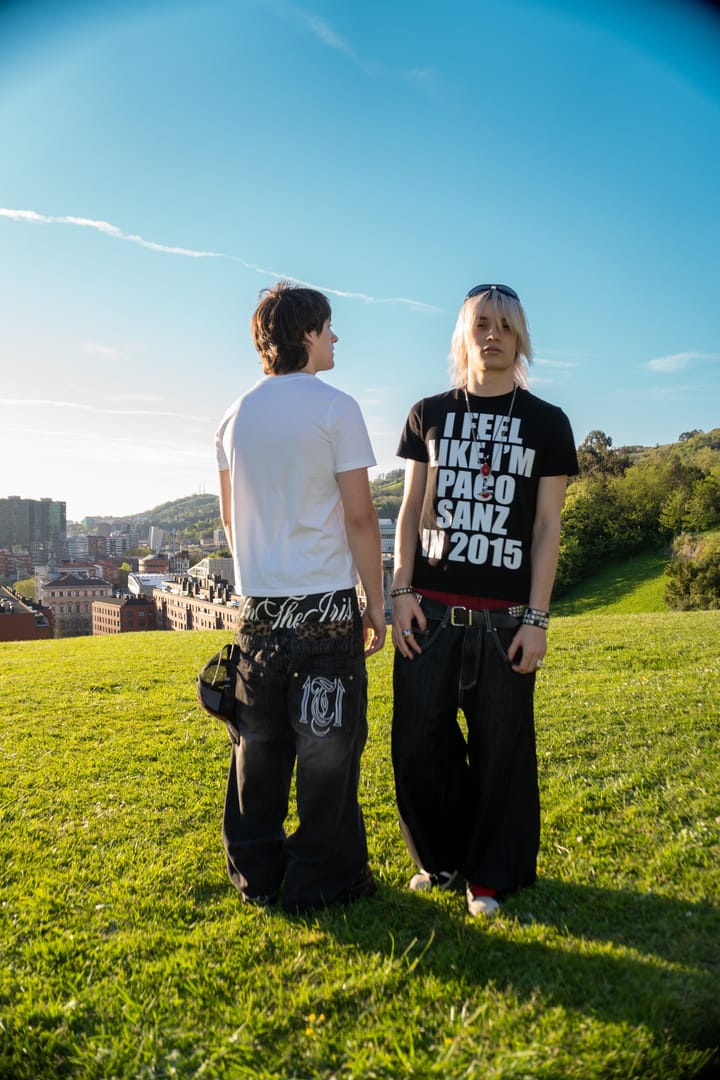 Un chico con la camiseta negra I feel like I’m Paco Sanz in 2015 junto a otro de espaldas, en un parque con Bilbao al fondo